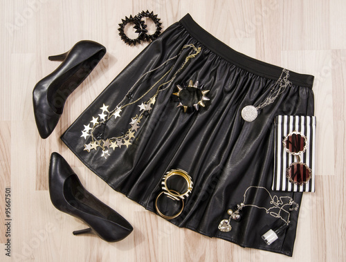 Black leather skirt and accessories arranged on the floor.Woman black and silver accessories, high heels shoes, necklace, bracelets and nail polish.