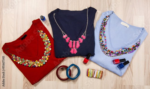 Winter sweaters and accessories arranged on the floor. Woman colorful accessories, necklace, bracelets and nail polish.