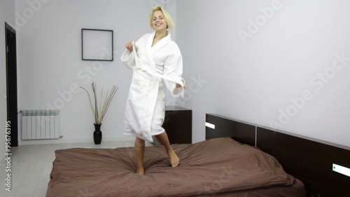 woman in bathrobe dancing on bed, young pretty girl smile undressing