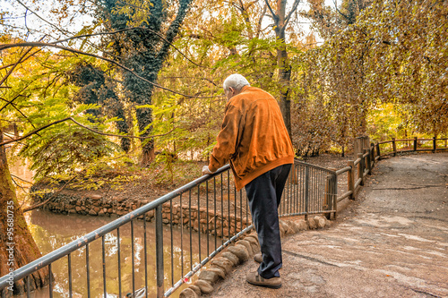 Senior leaning against railing watching  pond