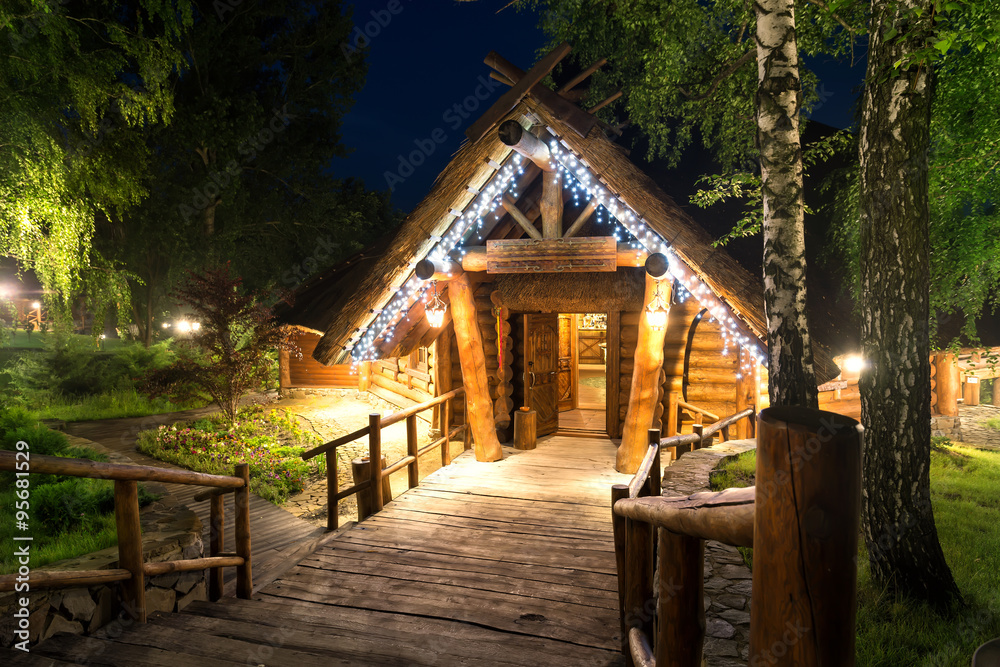 Fototapeta premium Wooden cottage in forest lit by lanterns