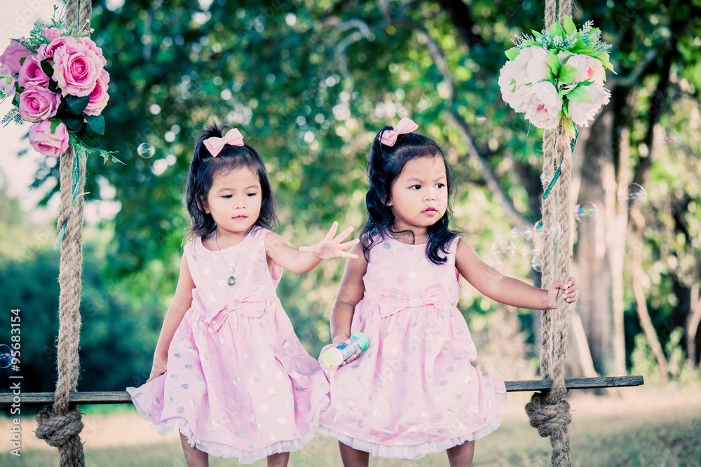 Children two cute little girls sitting on swing