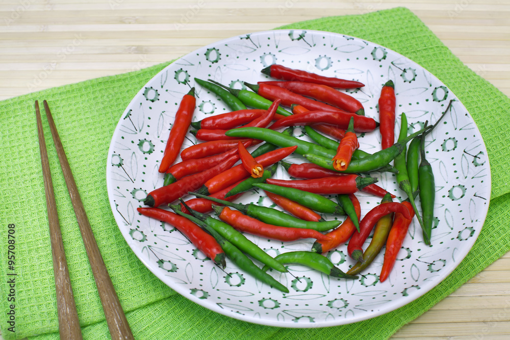 Decorative composition with chili pepper on a plate and chopsticks on table-napkin over bamboo background. Image of natural materials. Eco style. Decorative composition with chili pepper on a plate and chopsticks on table-napkin over bamboo background. Image of natural materials. Eco style.