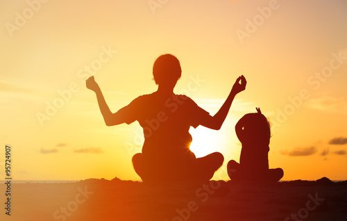 father and little daughter doing yoga at sunset