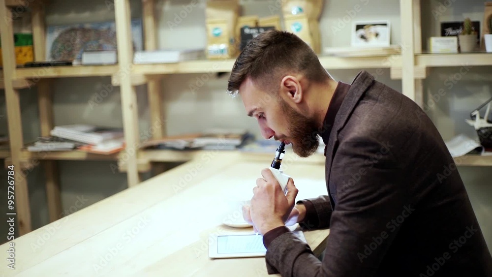 businessman in a suit reading on tablet with an e-cigarette vape businessman in a suit reading on tablet with an e-cigarette vape