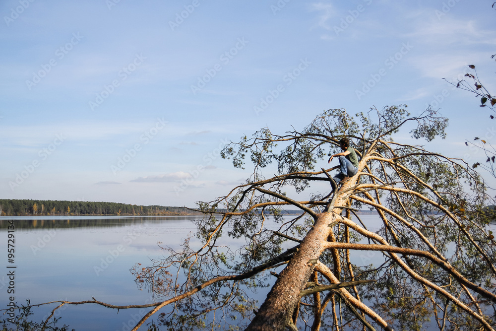 man standing on fallen tree over the lake