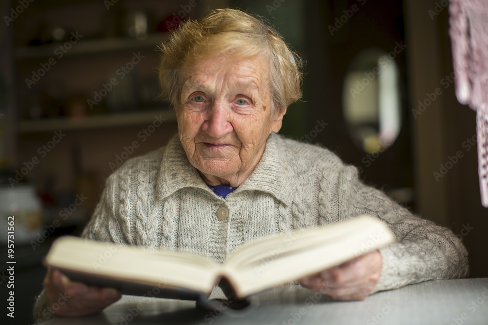 An old woman sitting at a table with a book.
