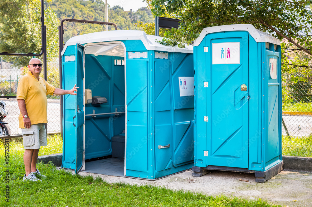 Blue portable toilet cabins in the park with a man of entrance. Blue portable toilet cabins in the park with a man of entrance.
