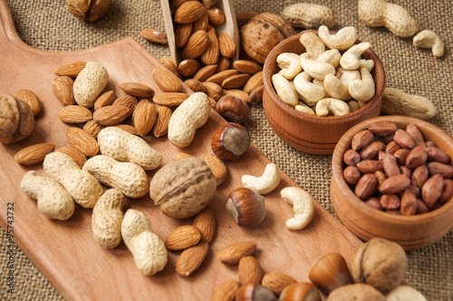 Almonds, cashew, walnuts and hazelnuts in wooden bowls on wooden board and burlap, sack background
