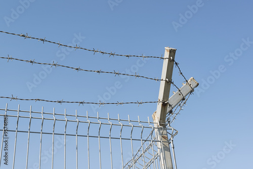 Metal border fence. Metal grid fence with barbed wire on the top.
