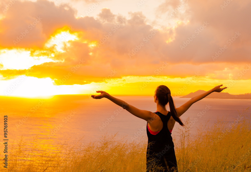 Sport and life achievements and success concept.. Sporty girl raising arms towards beautiful glowing sunshine.

