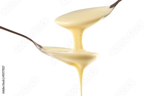 Condensed milk pouring from spoons, isolated on white