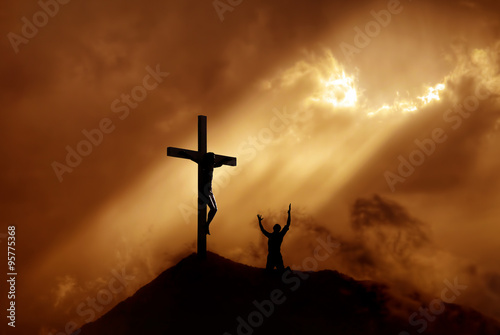 Fotografie, Obraz Dramatic sky scenery with a mountain cross and a worshiper