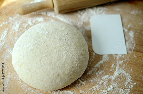 Whole wheat pizza dough ball with a rolling pin and a scraper on a floured working surface