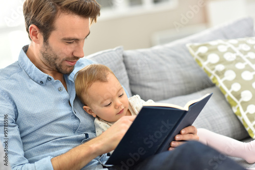 Father and child reading book in sofa