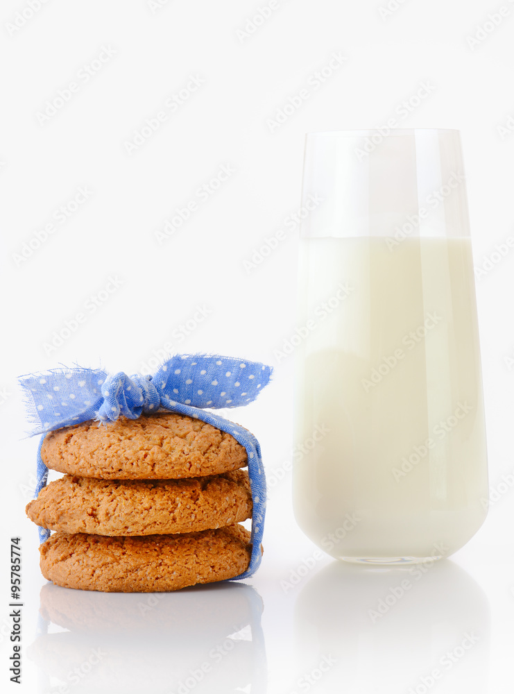 Stack of three homemade oatmeal cookies tied with blue ribbon in small white polka dots and glass of milk, isolated on white background Stack of three homemade oatmeal cookies tied with blue ribbon in small white polka dots and glass of milk, isolated on white background