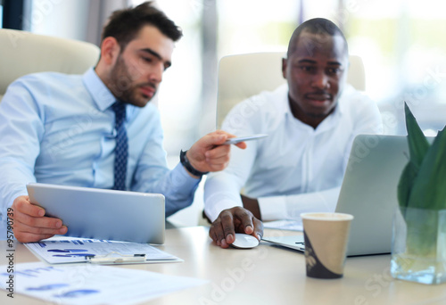 Image of two young businessmen interacting at meeting in office