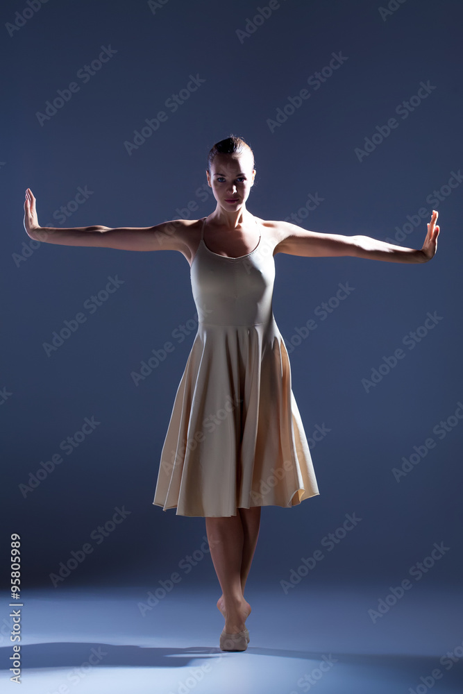 Young beautiful dancer in beige dress dancing on gray background Young beautiful dancer in beige dress dancing on gray background