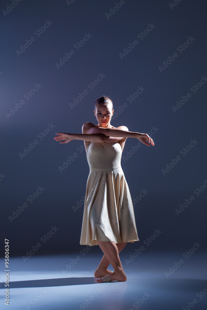 Obraz premium Young beautiful dancer in beige dress dancing on gray background