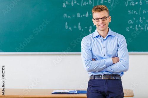 Young male professor is posing at the desk. 