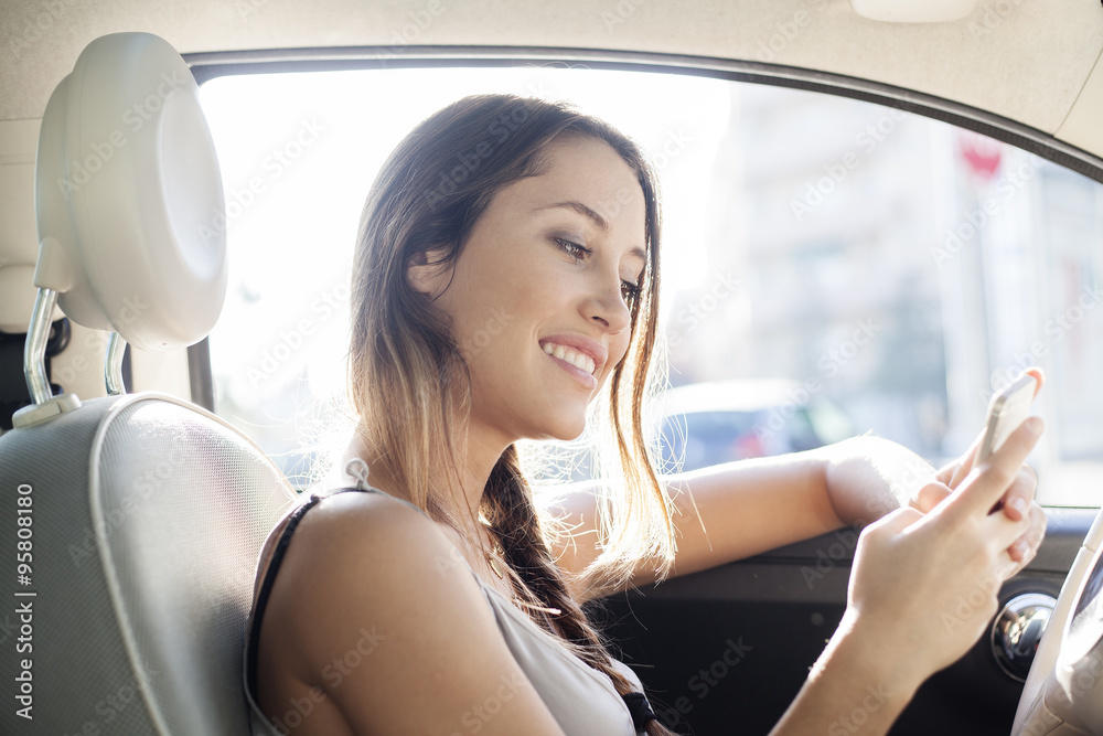 Young woman sending a message with her mobile phone sitting in her car Young woman sending a message with her mobile phone sitting in her car