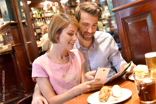 Couple of tourists in restaurant looking at map and smartphone