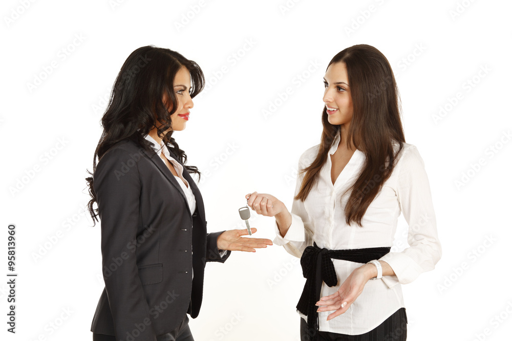 One woman presents a key to another woman in business attire.