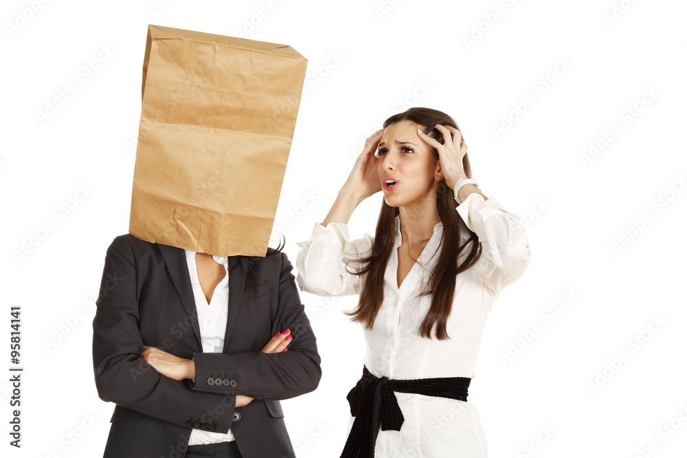 Two businesswomen. One talking in frustration, the other has a bag over her head.