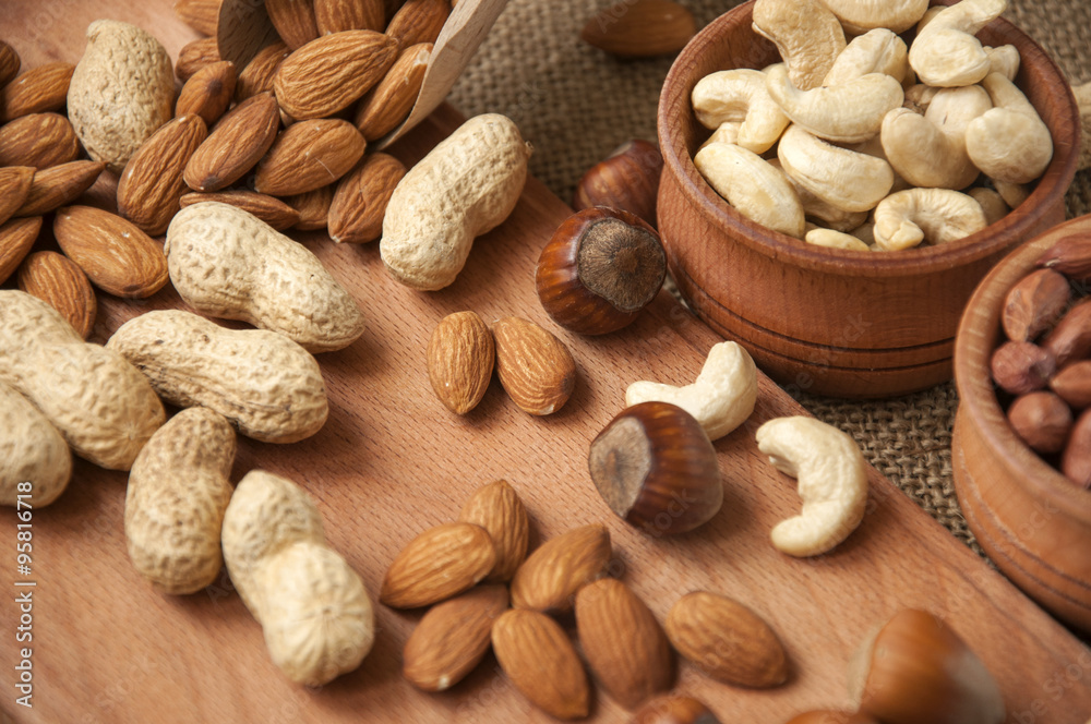 Obraz premium Almonds, cashew and hazelnuts in wooden bowls on wooden and burlap