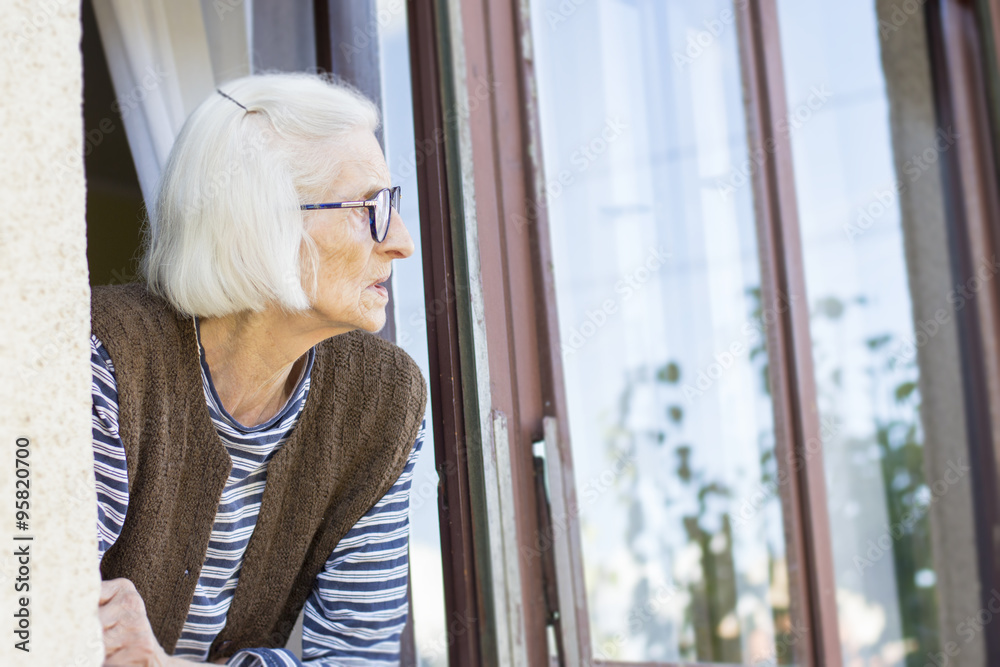 Fototapeta premium Old lady looking outside through her window