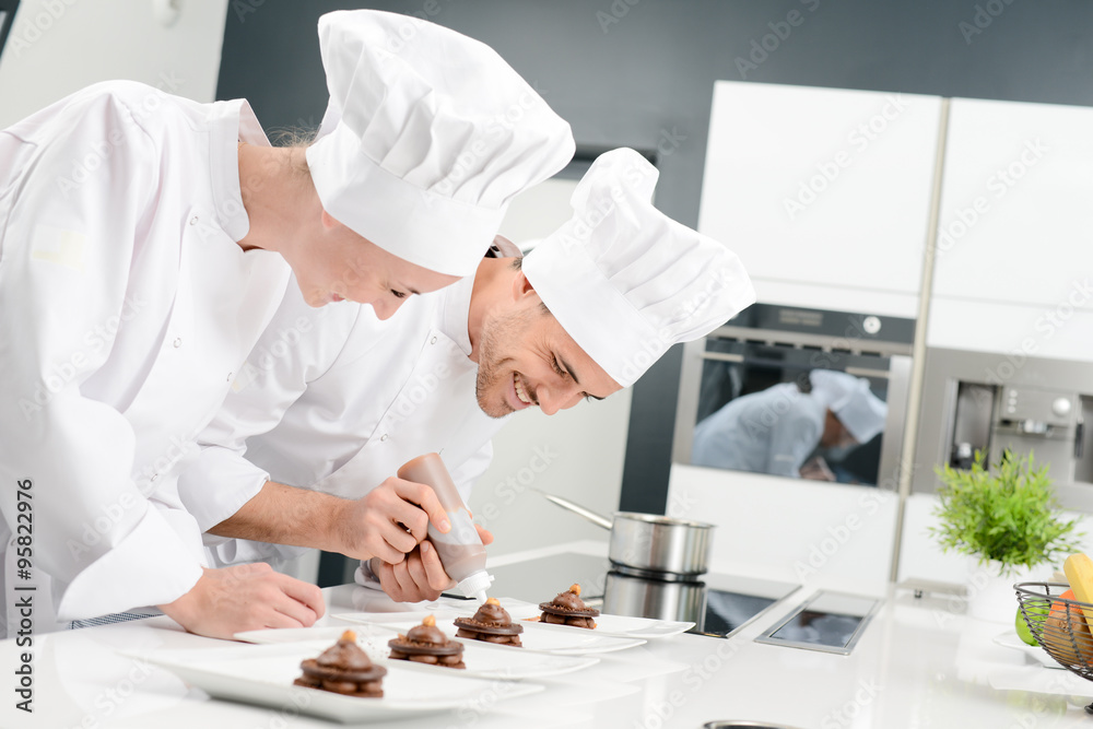 student and teacher in a professional cook school kitchen preparing a chocolate dessert