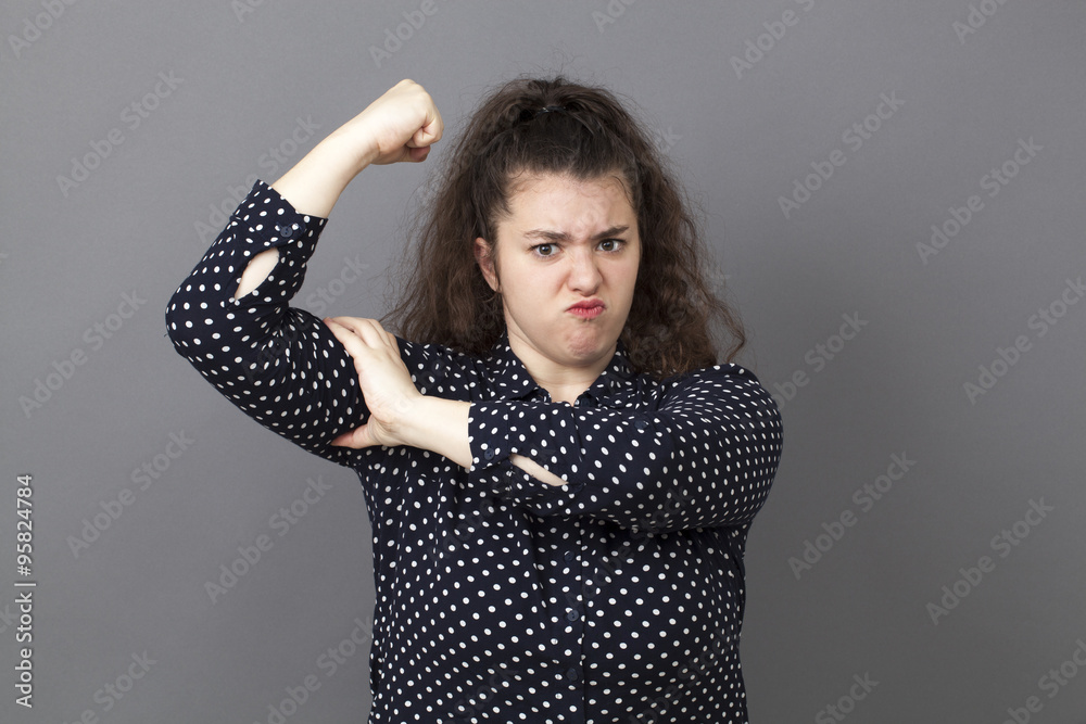 girl power concept - pouting big young brunette showing her muscular arm for feminine independence,studio shot girl power concept - pouting big young brunette showing her muscular arm for feminine independence,studio shot