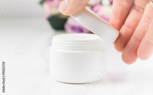Die rechte Hand einer Frau öffnet eine weiße Cremedose.