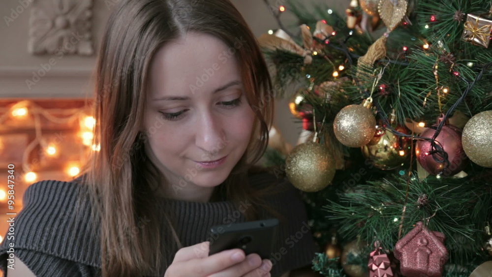 Woman using her mobile phone at christmas at home in the living room