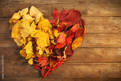 Colourful autumn leaves in the shape of heart, on wooden background