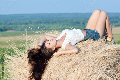 young beautiful long haired girl posing in shorts lying on a haystack. 