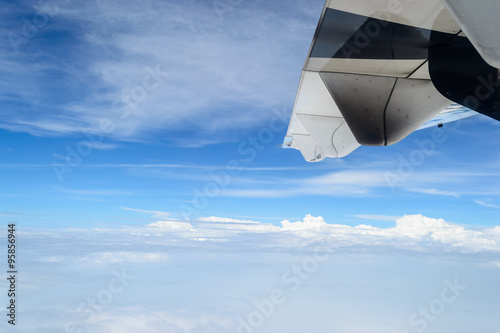 Wing of airplane flying above the clouds and blue sky