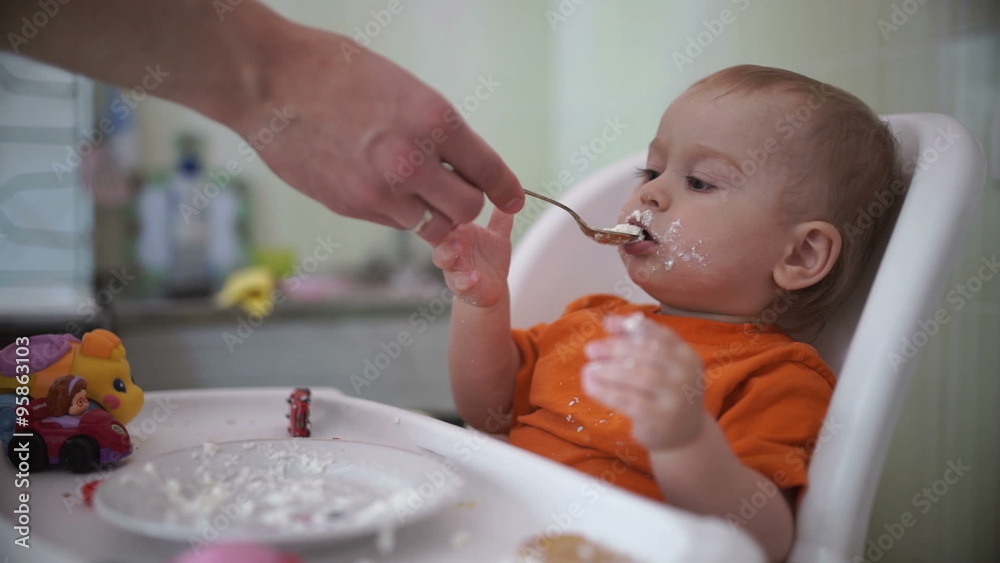 A boy sitting on the child seat and learn to eat independently.He eats cookies with a spoon cottage cheese. A boy sitting on the child seat and learn to eat independently.He eats cookies with a spoon cottage cheese.