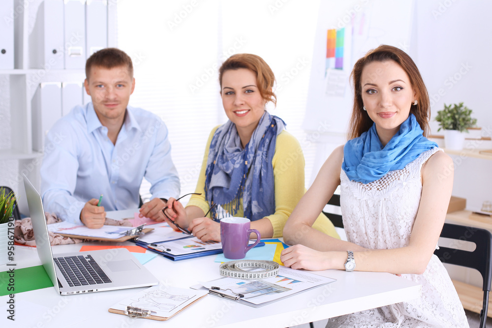 Portrait of attractive designers sitting on desk in office Portrait of attractive designers sitting on desk in office
