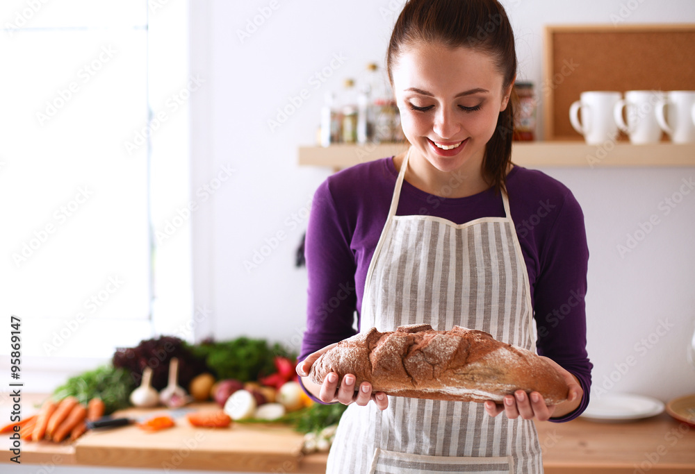 Young woman holding tasty fresh bread in her kitchen