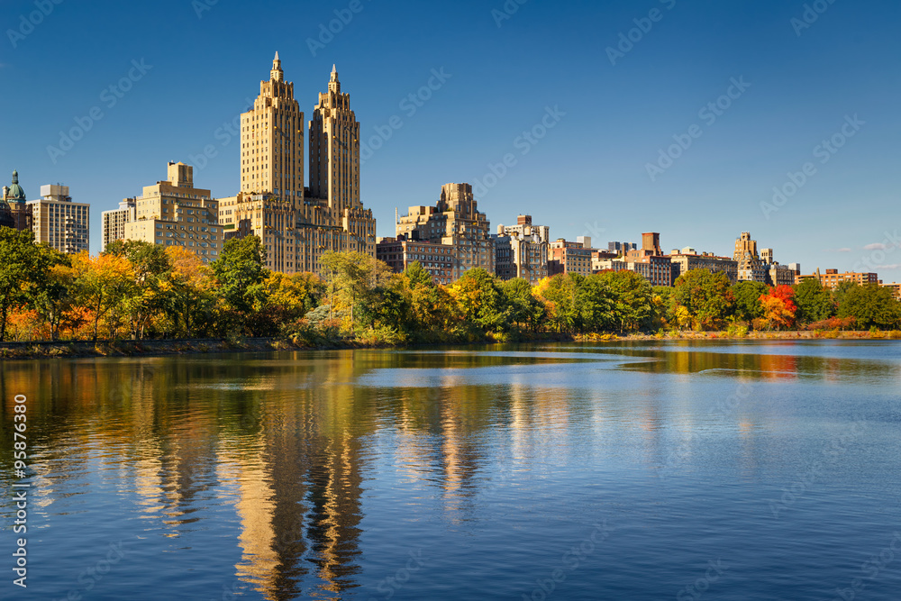 Fototapeta premium Central Park and Manhattan, Upper West Side with colorful Fall foliage. A clear blue sky and buildings of Central Park West reflecting in the Jacqueline Kennedy Onassis Reservoir. New York City.