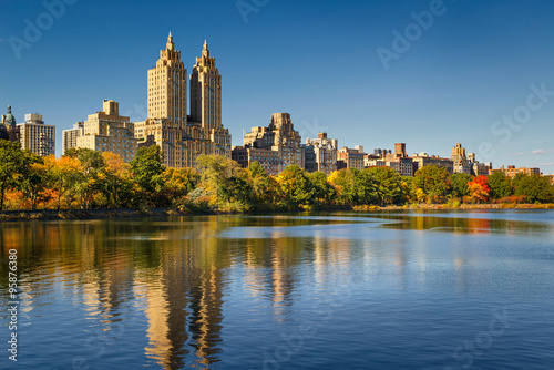 Fototapeta Naklejka Na Ścianę i Meble -  Central Park and Manhattan, Upper West Side with colorful Fall foliage. A clear blue sky and buildings of Central Park West reflecting in the Jacqueline Kennedy Onassis Reservoir. New York City.