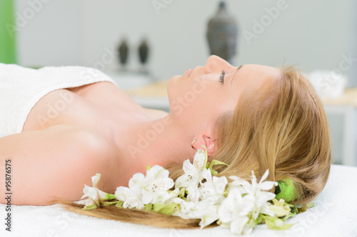 Beautiful woman wrapped in a towel laying in spa with white flow