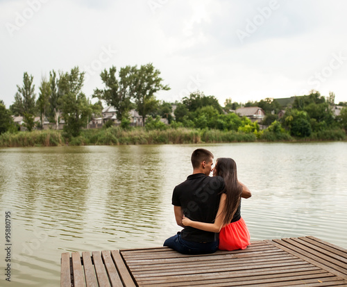 Rear view of a romantic young couple sitting on a jetty.