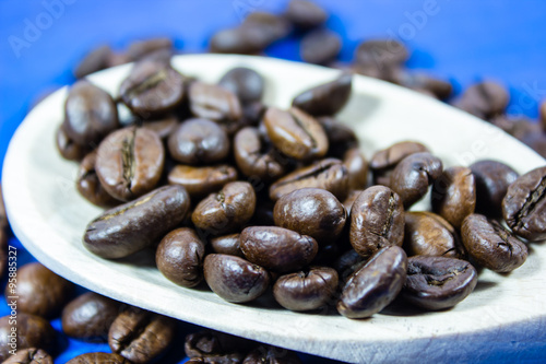 Coffee beans in wooden spoon on blue background photo