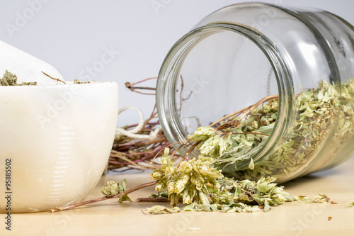 An overturned crystal pot with dry leaves of oregano beside marble mortar and pestle with dried leaves of pennyroyal