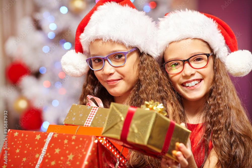 Happy sisters holding gifts in front of christmas tree Happy sisters holding gifts in front of christmas tree