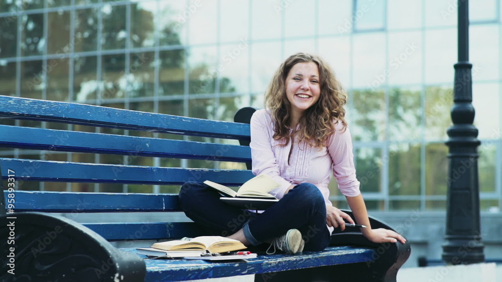 portrait of a happy female student sitting on a bench with books slow motion portrait of a happy female student sitting on a bench with books slow motion