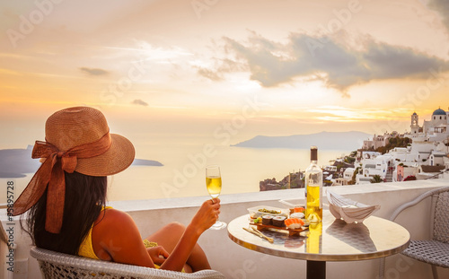 Female tourist enjoying food, wine and sunset view at Santorini, Greece