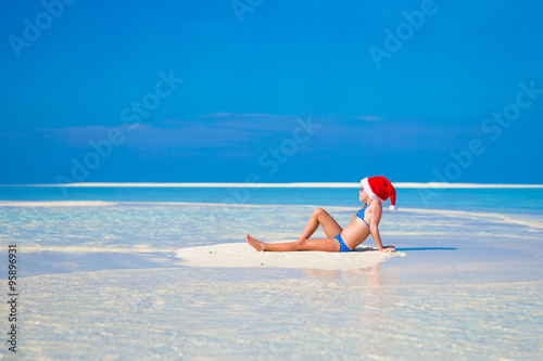 Little cute girl in Santa hat on white beach during vacation